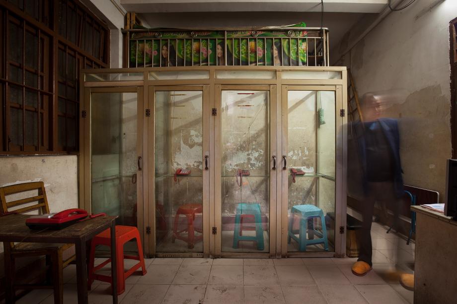 A shopkeeper stands near a bank of phone booths in Sanyuanli Village, Baiyun, Guangzhou, China