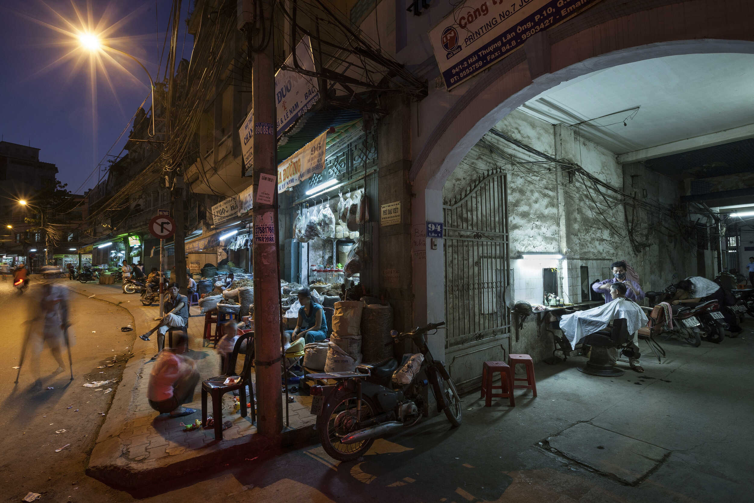 Editorial photograph of an alleyway barbershop along a street lined with traditional herb shops in Cholon, Ho chi Minh City, Vietnam.