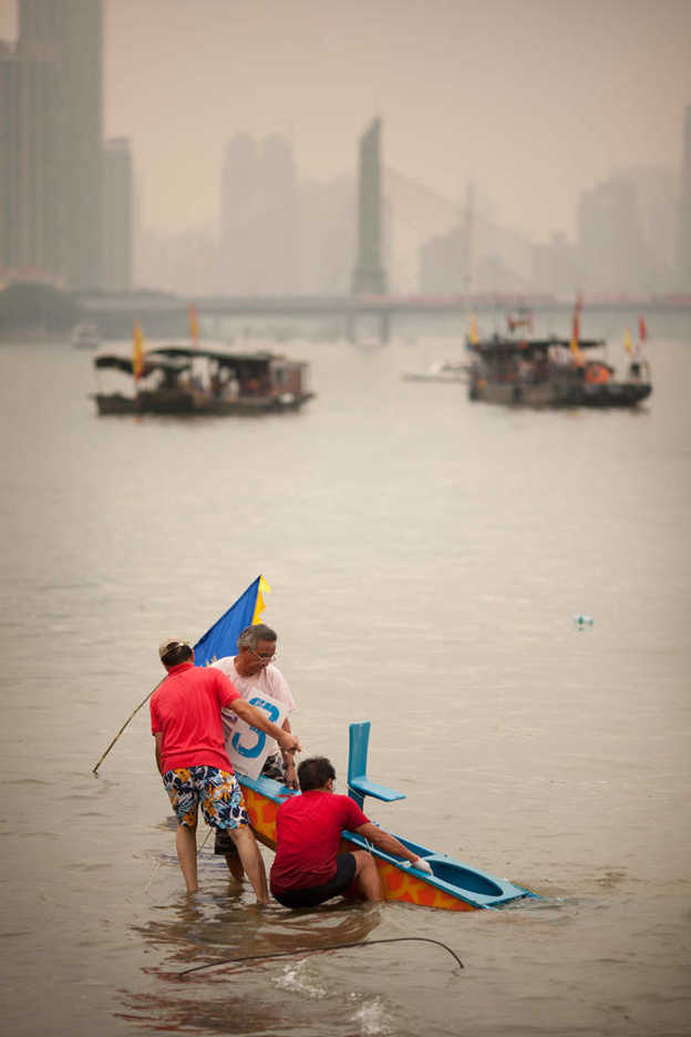 Three men pull a sunken dragon boat out of the pearl river in Guangzhou, China