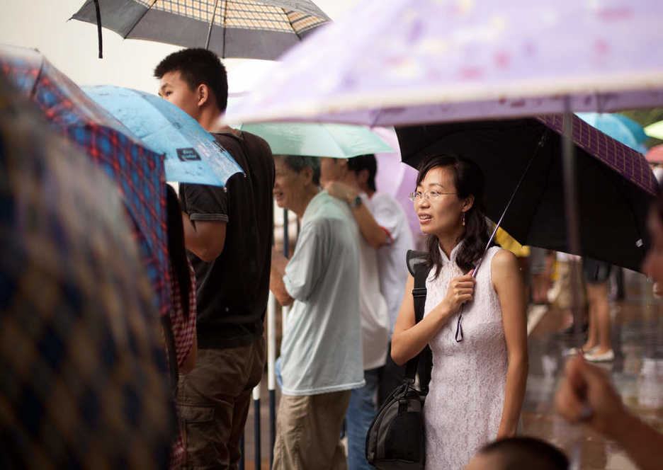 Elegantly dressed woman watches for dragon boats amidst a sea of umbrellas