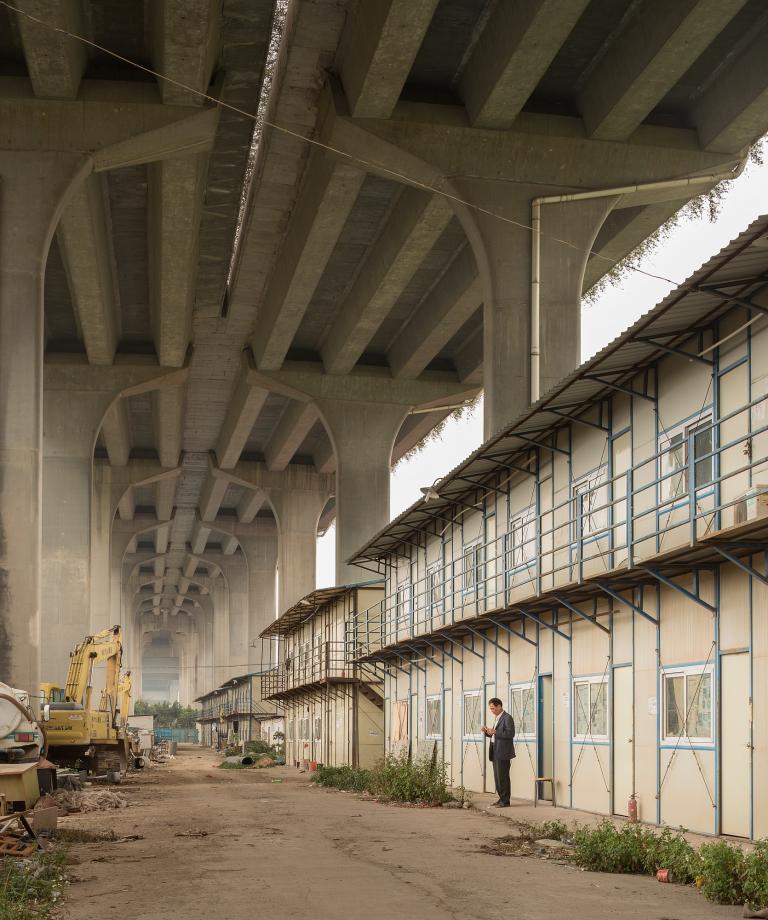 A man stands outside temporary worker housing under the Xinguang Expressway near Nanzhou Road in Haizhou District, Guangzhou