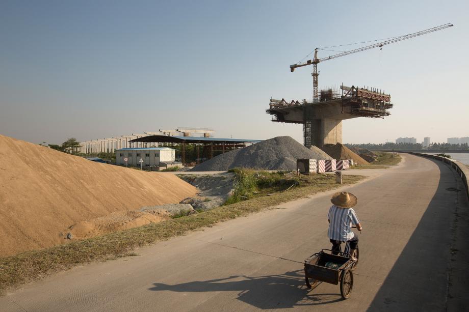A man rides a tricycle near a bridge under construction in Panyu